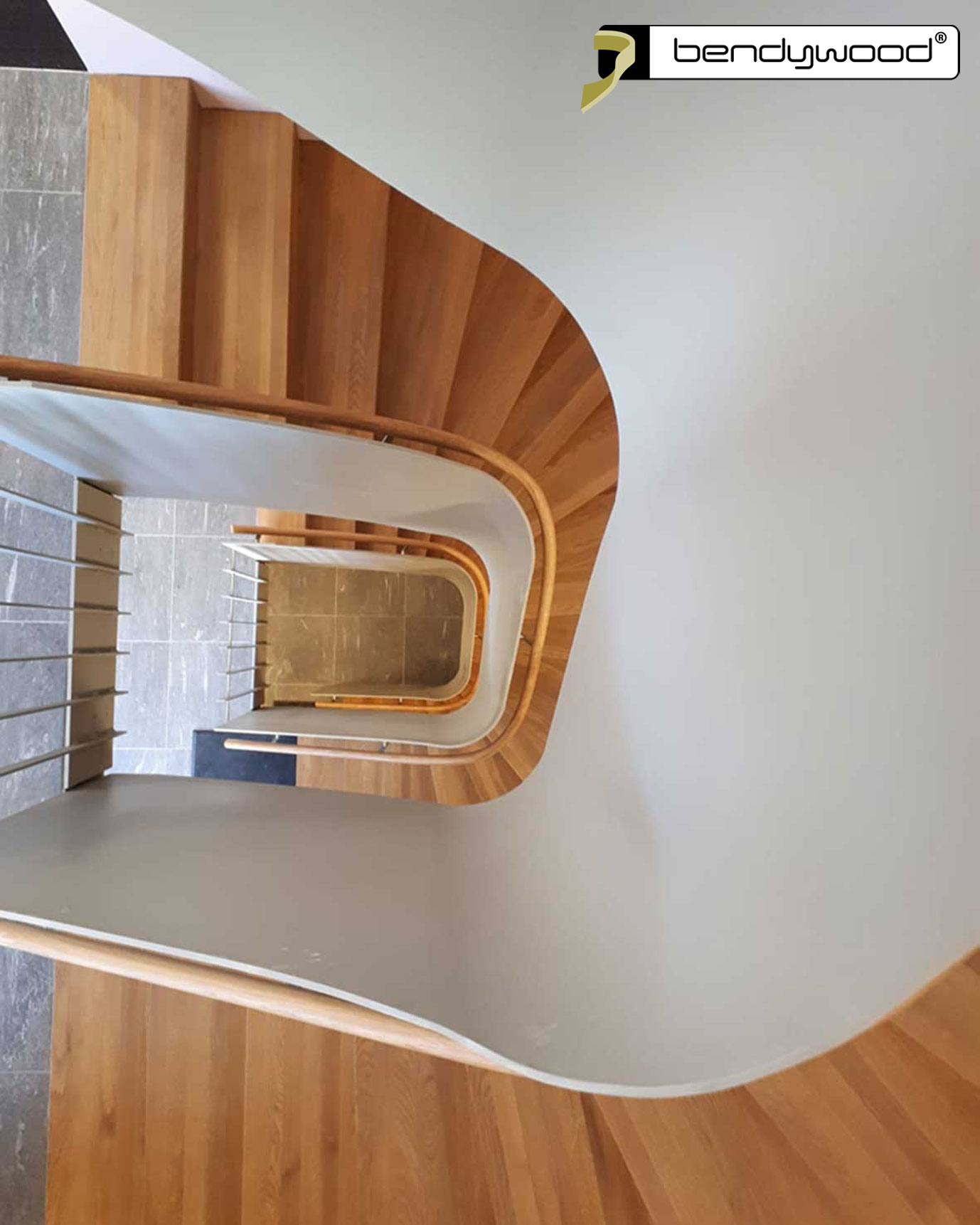 Corrimano rotondi in rovere Bendywood® per una scala curva con balaustra in lamiera di acciaio. 